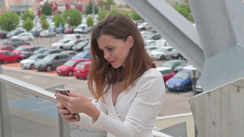 Beautiful woman with white sweater and black pants using mobile phone.