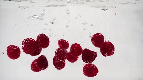 A beautiful ripe raspberry is immersed in a container of water with bubbles in slow motion. Theme of vegetarian and raw food as a lifestyle. Fruit cocktail.