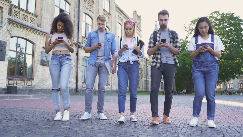 Group of no talking people walking at the street. Each one holding smartphone, texting, web searching. Communication problem, 21 century problem. Handheld shot.