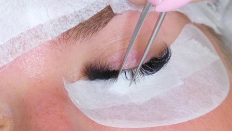 Close up eyelash extension Procedure. Eyelash extension master glues long artificial eyelashes to the woman client in beauty salon. 4k footage.