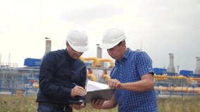 teamwork. industry gas production station concept. slow motion video. two engineers in helmets are studying working with a digital tablet in factorygas supply business contract. two workers work at