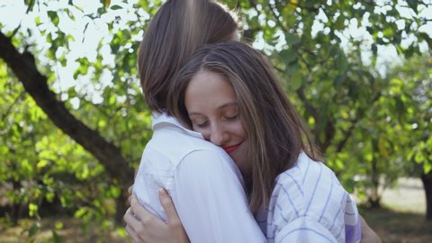 Happy young man and woman hugging and smiling happily while standing in park or garden. Leisure outdoors, connecting with nature. Camera moving around