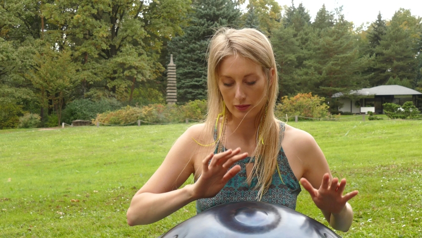 Girl plays in the green field on a hangdrum