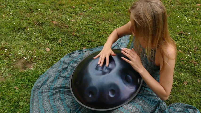 Girl plays in the green field on a hangdrum