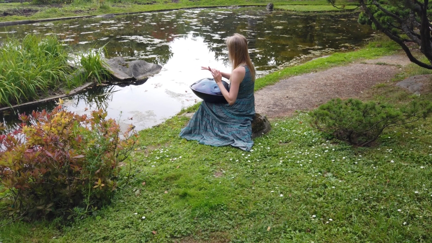 Beautiful young woman plays a hangpan in the autumn park
