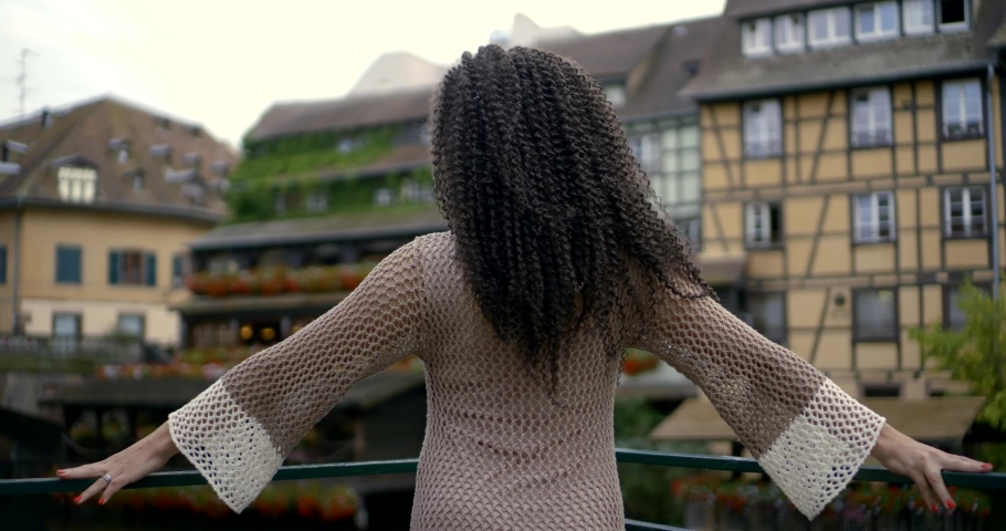 Beautiful young attractive American woman with curly hair in knitted wool clothes with her back to the camera and a spread on the background with a European city