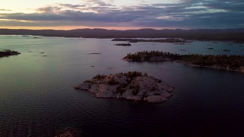 Rocky Granite Islands with Green Pine Trees in Blue Lake at Sunset, Drone Aerial Wide Orbit Pan. Flying over Wild Natural Georgian Bay Waves with Far Mountains at Golden Hour in Ontario Canada