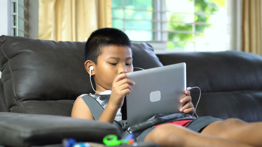 Asian boy playing tablet on sofa, Upload or download bar with percent, remaining time countdown.
