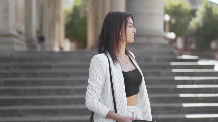 Stylish businesswoman dancing on the streets listening to music, medium shot