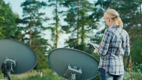 Rear view of Woman tunes satellite dishes outdoors, uses tablet