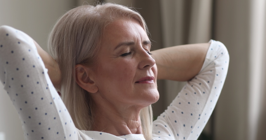 Happy relaxed dreamy middle aged older woman relax hold hands behind head sitting at home, calm mature adult lady smiling face rest dream alone enjoy comfort stress free peace of mind, close up view Royalty-Free Stock Footage #1037252531