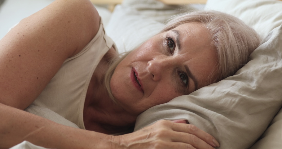 Annoyed middle aged mature woman feel frustrated suffer from insomnia uncomfortable bad mattress lying awake in bed, upset senior old lady insomniac trying to sleep disturbed toss and turn in bedroom | Shutterstock HD Video #1037252546