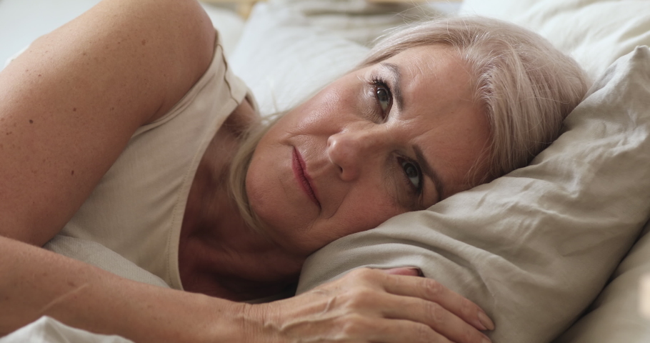 Annoyed middle aged mature woman feel frustrated suffer from insomnia uncomfortable bad mattress lying awake in bed, upset senior old lady insomniac trying to sleep disturbed toss and turn in bedroom | Shutterstock HD Video #1037252546