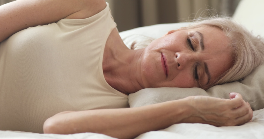 Calm serene healthy mature middle aged woman resting alone sleeping well in comfortable bed lying asleep on soft pillow relax on orthopedic mattress enjoy good night sleep concept, close up view Royalty-Free Stock Footage #1037252558