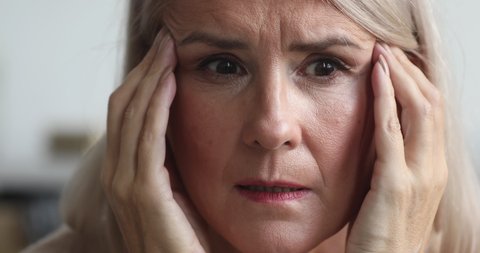 Close up view of scared upset middle aged older woman feeling afraid stressed face thinking of disease or mental problems having strong headache suffer from panic attack or memory loss concept