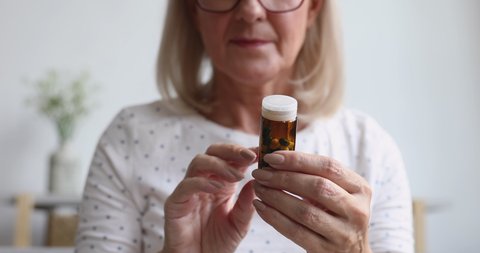 Sick ill old senior woman hold painkiller pill bottle read prescription side effect take medicine meds to relieve pain in mature grandma hands, older people pharmacy medicament concept, close up view