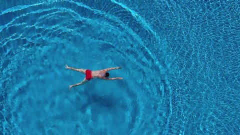 View from the top as a man dives into the pool like a bomb and swims under the water