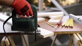 Adult craftsman carpenter with his hands protected by gloves works with the electric saw to cut a wooden table. Housework, do it yourself. Footage.