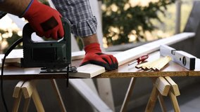 Adult craftsman carpenter with his hands protected by gloves works with the electric saw to cut a wooden table. Housework, do it yourself. Footage.