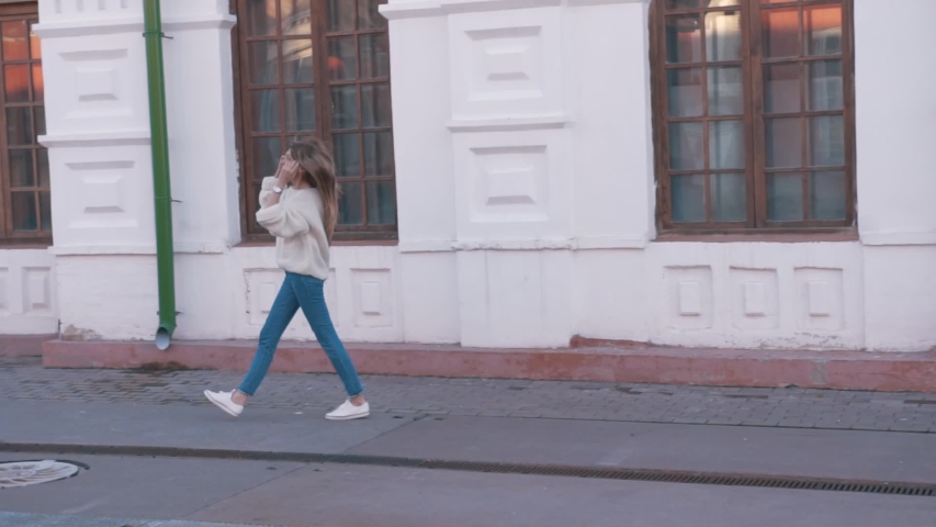 pretty slender girl is filled with joy and positive emotions. girl in jeans and a knitted oversized sweater walks the streets of the city and smiles at the camera