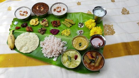 Video of traditional Indian lunch Onam sadhya, boiled rice served on green banana leaf with many spicy hot curries and lots of sweet dessert for Kerala harvest festival in India. Silk saree background