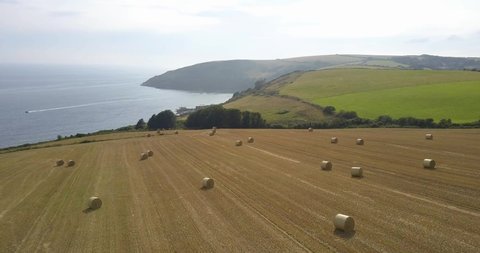 Aerial footage flying over Cornish coastline, fields and hay bales at Looe, Cornwall, UK