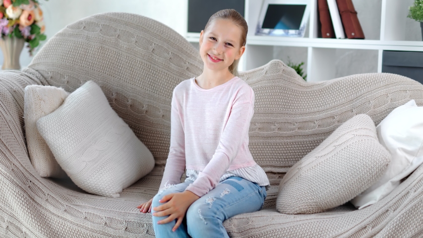 Smiling attractive European female children posing sitting on couch looking camera