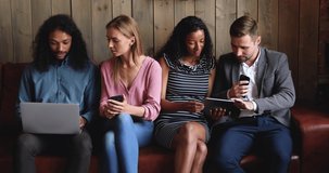 Multiracial friends group share social media news sit together talk hold devices, smiling diverse young students communicate using apps on phones laptop digital tablet, people and technology concept