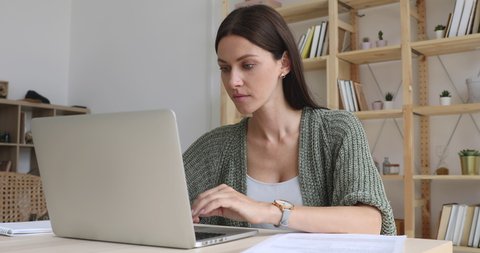 Focused businesswoman doing paperwork working online on laptop sit at home office desk, female entrepreneur professional freelancer using computer software pay bills in app typing at modern workplace