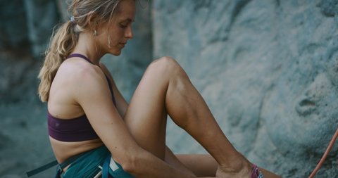Fit woman putting on her rock climbing shoes preparing to rock climb, cinematic rock climbing moments