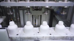 White plastic bottles passing along a conveyor belt are filled with liquid by special production press. Manufacturing packaging process Close-up, looped video, UHD 4K