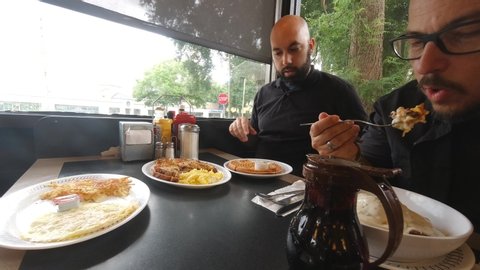 Three guys eat breakfast at an undefined restaurant. They enjoy waffles, eggs, and hashbrowns. Shot in 4k timelapse.