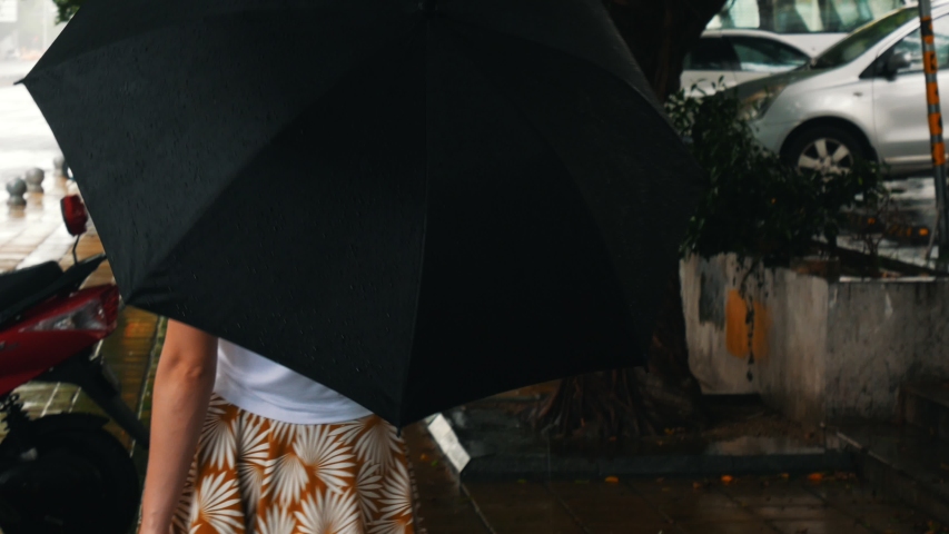 A young woman walking on the street during the rain holding an umbrella