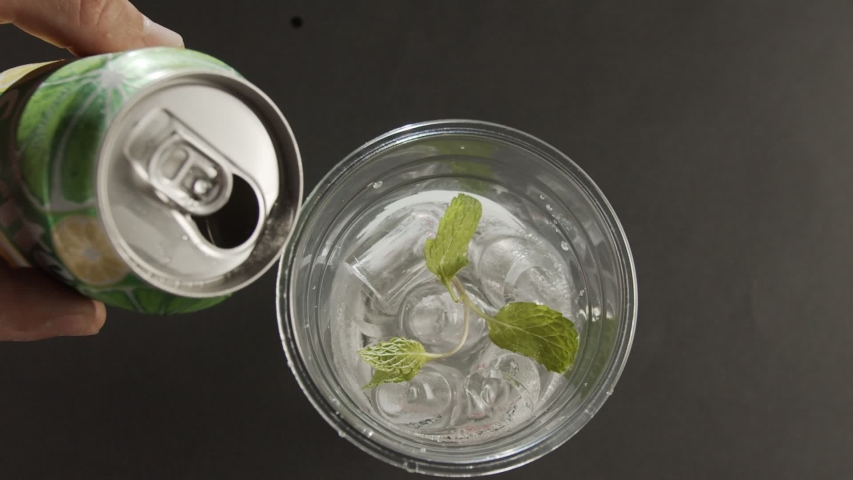 Top view in glass with ice and mint pours coda from metal can. Slow motion video
