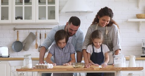 Happy family mom dad and kids siblings helping preparing dough with rolling pin together, young parents teaching children son daughter learning cooking in modern kitchen baking pastry at home