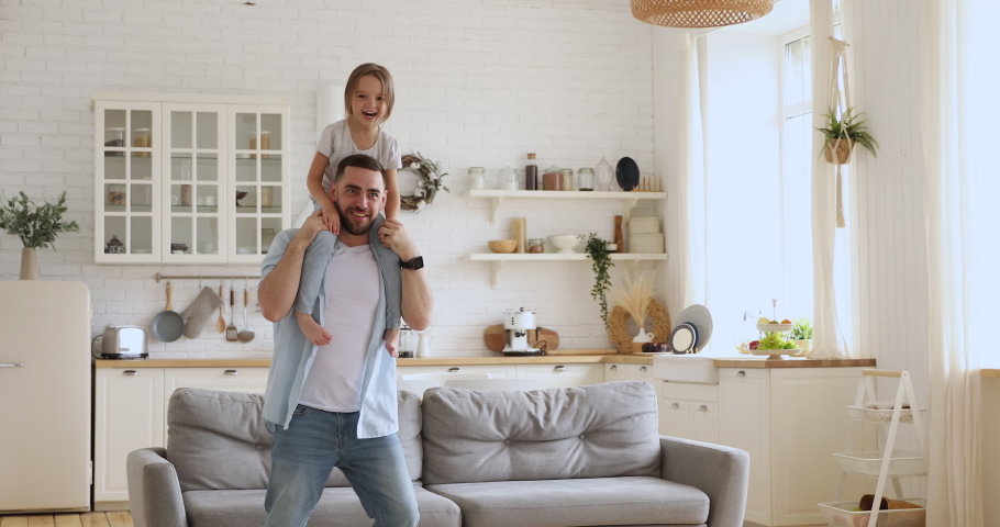 Loving young dad carrying cute little kid daughter giving piggyback ride at home, happy funny small girl sitting on father shoulder playing carrying child bonding having fun laughing in kitchen room Royalty-Free Stock Footage #1037333513