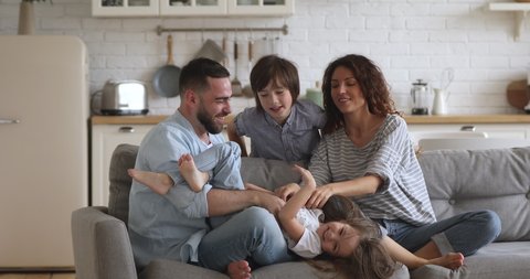 Happy family of four mum dad with cute little children son daughter tickling laughing on sofa together, parents and small kids having fun play bonding at home enjoy funny lifestyle activity on couch