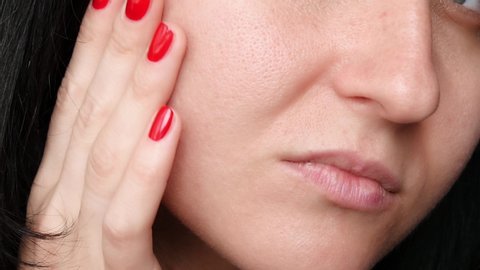 Female face close-up. Skin texture with enlarged pores. The girl touches the fingers of the problem skin of the face, considering it. The concept of care for problem skin, age-related changes