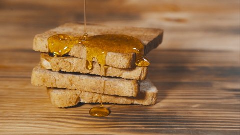 Pouring Honey on Toasts on Wooden Board. Slow Motion