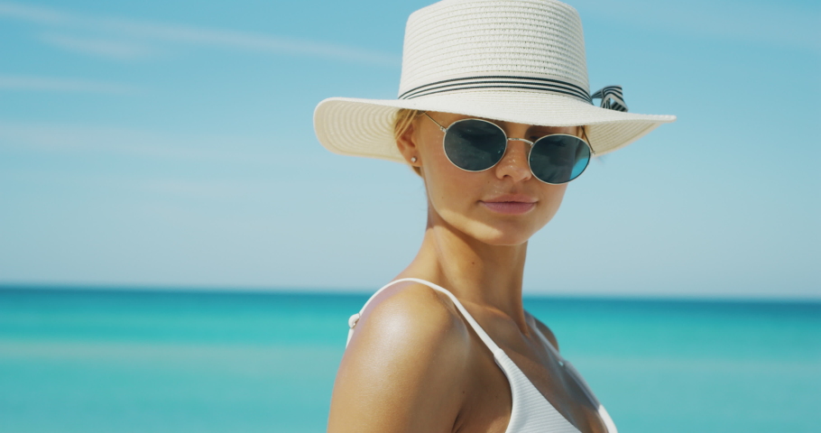 Slow motion of happy young blond hair woman with a hat and sunglasses is applying a sunscreen or sun tanning lotion to take care of her skin during a vacation on a beach and smiling in camera. Royalty-Free Stock Footage #1037348744