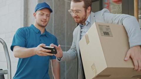 Delivery Man Gives Postal Package to a Business Customer, Who Signs Electronic Signature POD Device. In Stylish Modern Urban Office Area Courier Delivers Cardboard Box Parcel to a Man