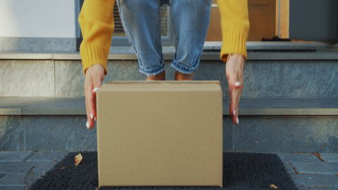 Contactless Delivery of Internet Ordered Goods, Cardboard Box Package on the Door Step, Anonymous Woman Walks out of the Front Door and Picks-up Her Postal Parcel. Safe No Contact Delivery