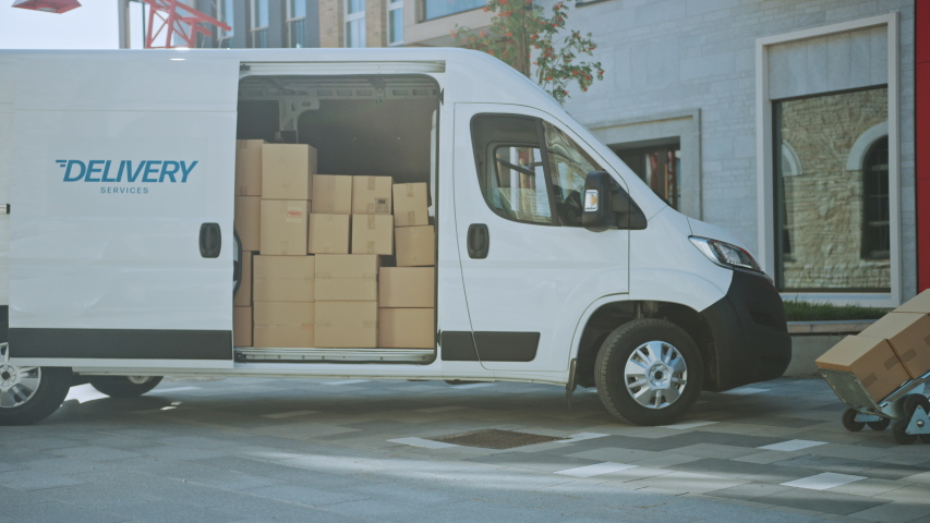 Delivery Man Uses Hand Truck Trolley Full of Cardboard Boxes and Packages, Loads Parcels into Truck / Van. Professional Courier / Loader helping you Move, Delivering Your Purchased Items Efficiently Royalty-Free Stock Footage #1037351195