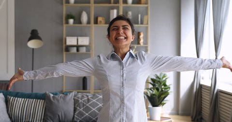 Happy overjoyed first time home owner young indian woman spin dance alone with arms outstretched in modern living room interior enjoy freedom having fun in new flat, investment, independence concept