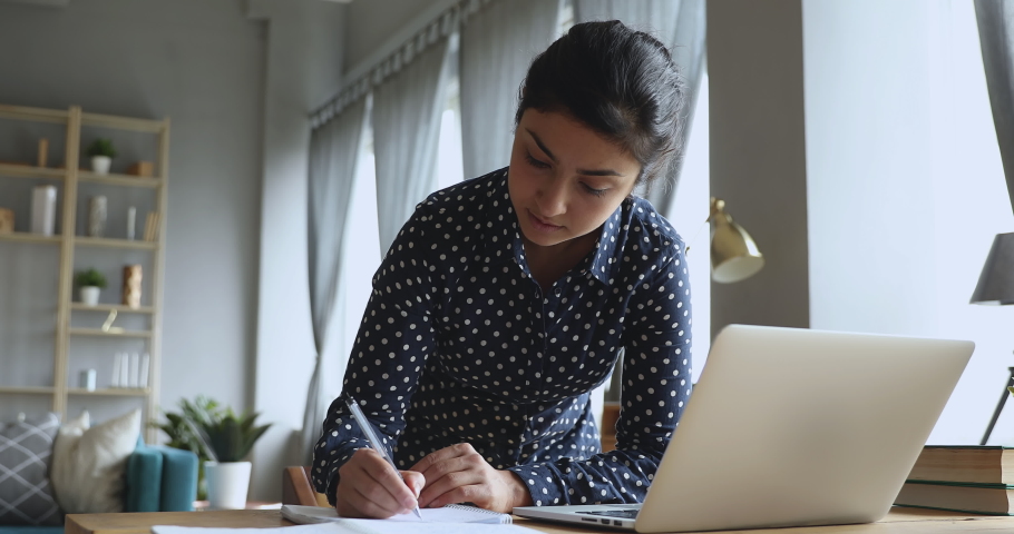 Focused indian girl university student studying on laptop writing notes, serious young woman prepare for test exam doing research project coursework homework learning at home using computer at desk Royalty-Free Stock Footage #1037352935