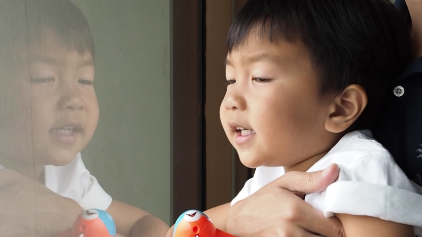 Asian child boy looking for plane through window at airport, hand holding and playing plane toy with happiness, freedom, relax time.Young kid in hug of dad. Happy family fun day in holiday.