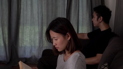 4K Dolly shot unhappy young asian couple sitting on sofa after quarrel fight at home and not talking together. Unhappy man and woman couple having a relationship conflict and thinking of break up.