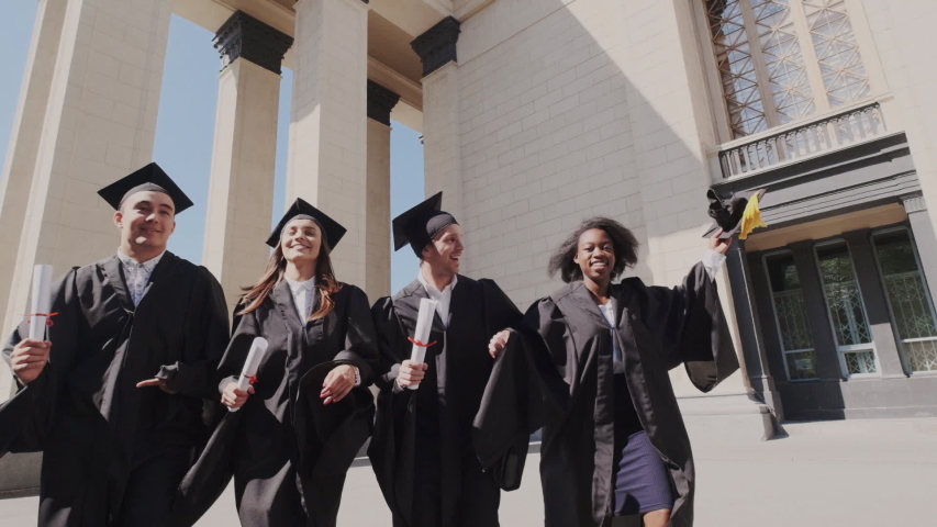Super slow motion. Celebrate approved examination in status educational institute. A group of happy and successful graduates running and have fun with diploma. Multi Ethnic, Mantle, academic caps.
