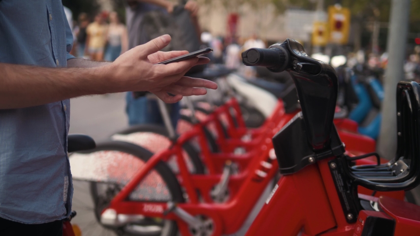 Tourist man take Electric Kick scooter or bike bicycle in sharing parking lot, tourist phone application. New sharing business project started in city, eco transportation Royalty-Free Stock Footage #1037365886