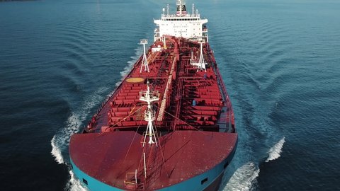 Bow and front deck of oil chemical tanker on ride. Low level track over tanker ship. Shot develops from open sea revealing ship bridge to wake water. Aerial close up of the bulbous bow breaking waves
